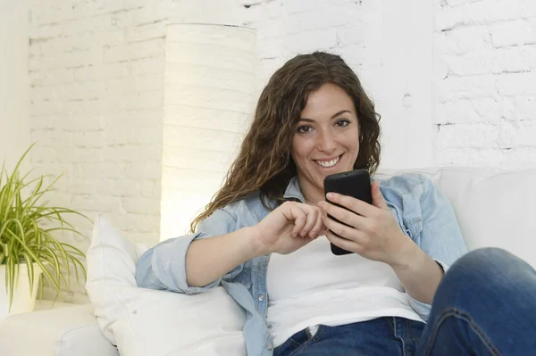 Young attractive spanish woman using mobile phone app or texting on home couch