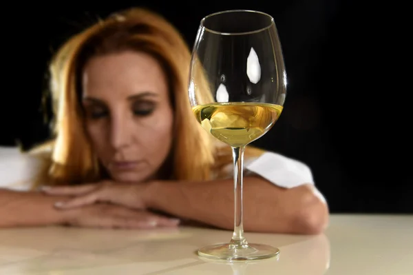 Drunk alcoholic blond woman alone in wasted depressed drinking white wine glass suffering hangover