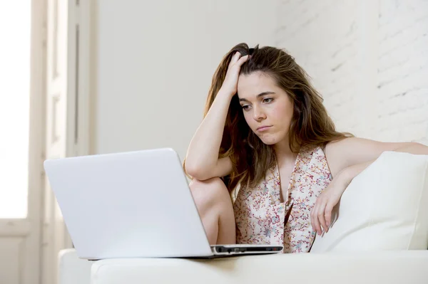 Disappointed girl at home couch using internet for studying with laptop computer