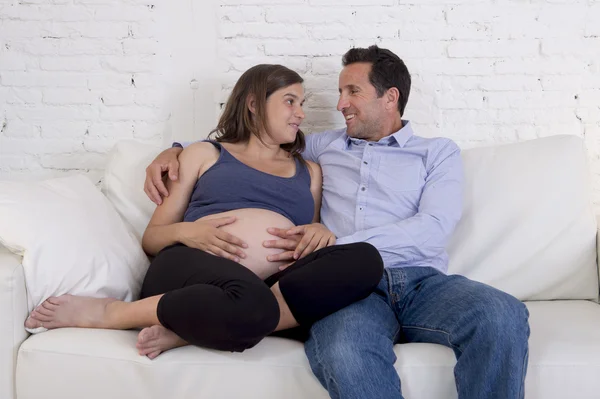 Young couple in love at home living room couch with the woman being pregnant