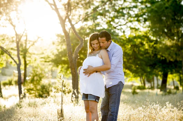 Young happy couple in love together on park landscape sunset with woman pregnant belly