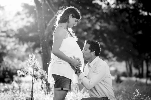 Young happy couple in love together on park landscape sunset with woman pregnant belly