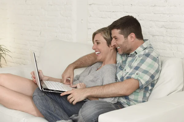Beautiful couple in love on couch together with laptop computer happy at home using internet