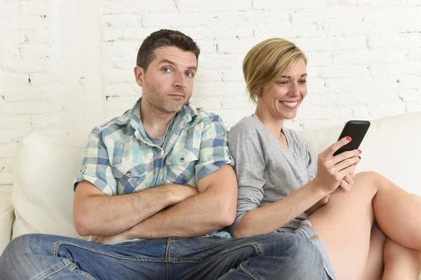 Attractive couple at home couch happy woman internet addict on mobile phone ignoring sad husband