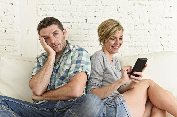 Attractive couple at home couch happy woman internet addict on mobile phone ignoring sad husband
