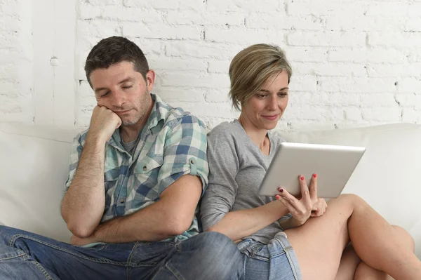 Couple with happy wife using internet app on digital tablet pad ignoring bored and sad husband