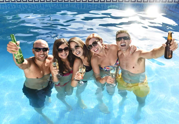 Happy attractive men and women in bikini having bath at hotel resort swimming pool drinking beer