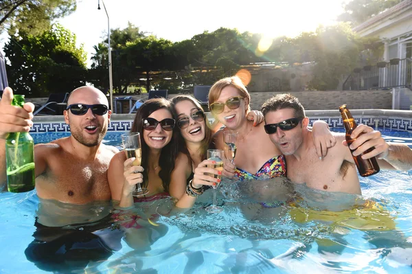 Happy attractive men and women in bikini having bath at hotel resort swimming pool drinking beer