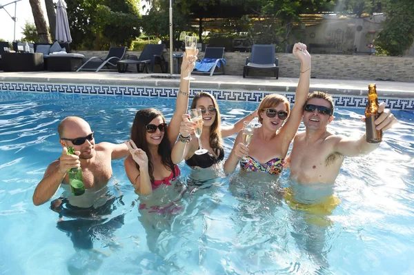 Happy attractive men and women in bikini having bath at hotel resort swimming pool drinking beer