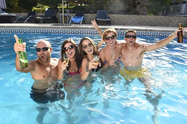 Happy attractive men and women in bikini having bath at hotel resort swimming pool drinking beer
