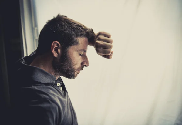 Attractive man leaning on window suffering emotional crisis and depression