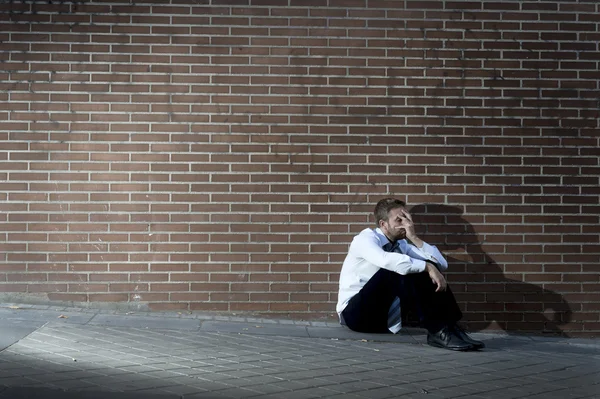 Businessman who lost job lost in depression sitting on city street corner