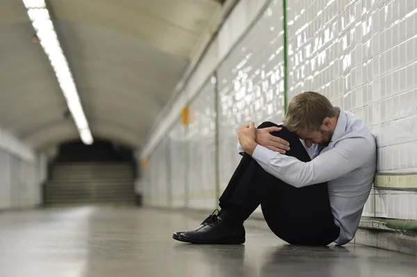 Young businessman lost in depression sitting on ground street subway
