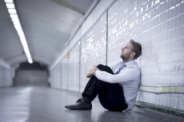 Young businessman lost in depression sitting on ground street subway