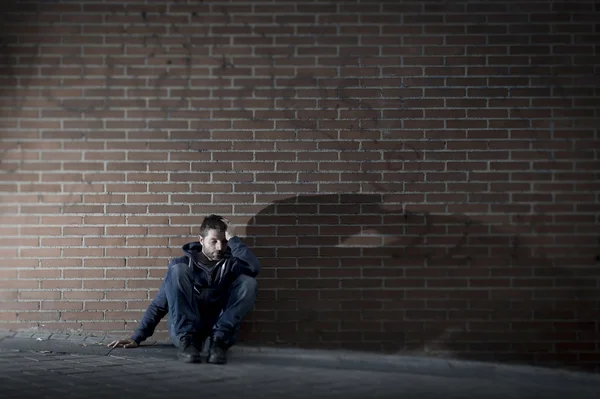 Young desperate man who lost job lost in depression sitting on ground street corner