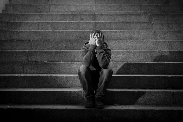 Young man lost in depression sitting on ground street concrete stairs