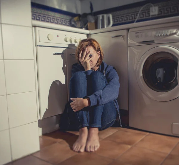 Lonely and sick woman sitting on kitchen floor in stress depression and sadness