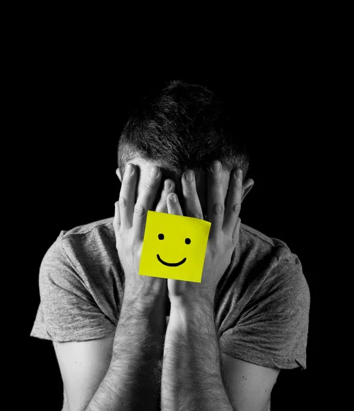 Young man suffering depression and stress alone with smiley face post it note