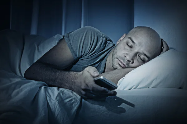 Young cell phone addict man sleeping at night in bed while using smartphone