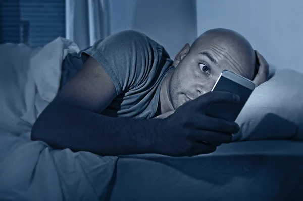 Young cell phone addict man awake at night in bed using smartphone