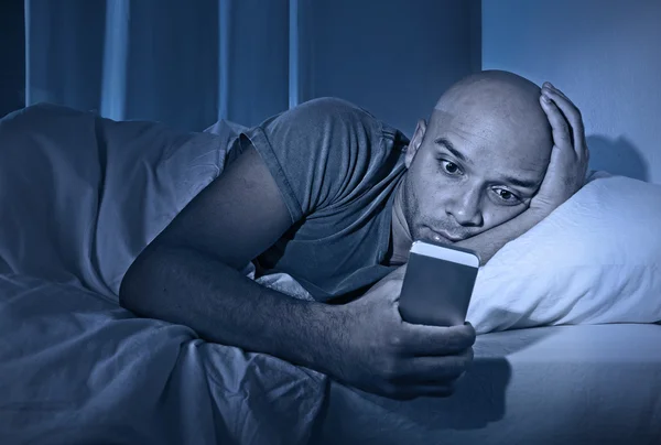 Young cell phone addict man awake at night in bed using smartphone