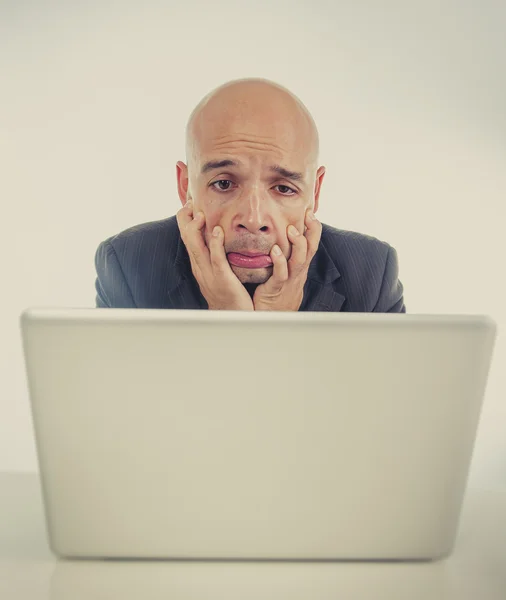 Hispanic businessman in stress at laptop holding monitor screaming desperate
