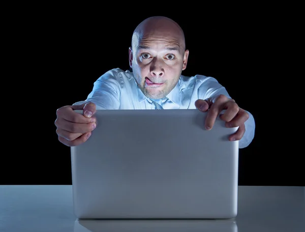 Businessman alone at night sitting at computer laptop watching porn or online gambling