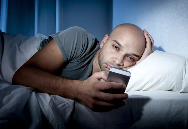 Young cell phone addict man awake at night in bed using smartphone