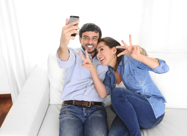 Nice attractive young couple sitting together in sofa couch taking selfie photo with mobile phone