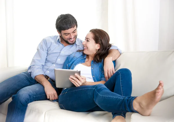 Young happy couple on couch at home enjoying using digital tablet computer