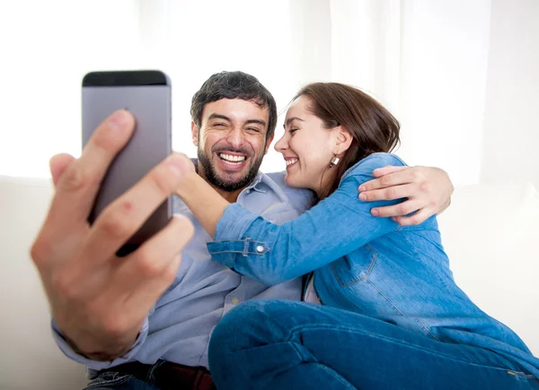 Nice attractive young couple sitting together in sofa couch taking selfie photo with mobile phone