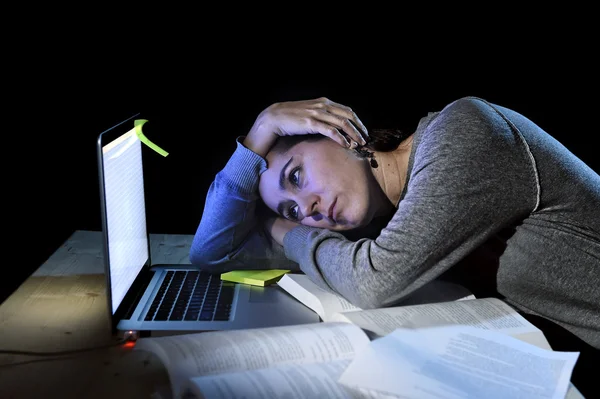 Young desperate university student girl in stress for exam studying with books and computer laptop late at night