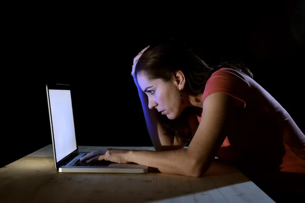 Young concentrated freelance worker or student woman working with computer laptop alone late at night in stress studying for exam