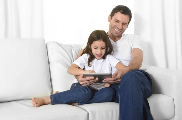 Young father sitting on couch with sweet little daughter using digital tablet smiling happy