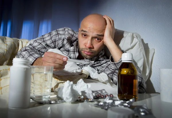 Sick man lying in bed suffering cold and winter flu virus having medicine and tablets