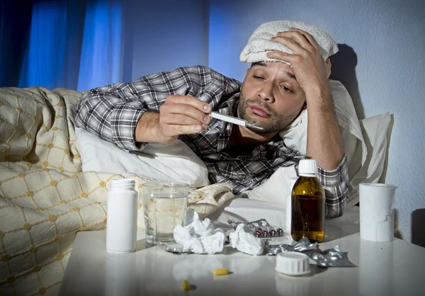 Sick man lying in bed suffering cold and winter flu virus having medicine and tablets