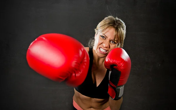 Young fit and strong attractive boxer girl with red boxing gloves fighting throwing aggressive punch training workout in gym feeling angry