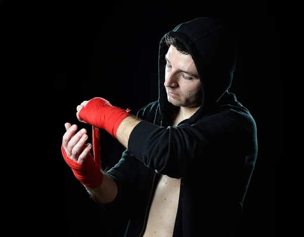 Man in boxing hoodie jumper with hood on head wrapping hands wrists before gym training