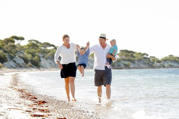 Young happy beautiful family walking together on the beach enjoying summer holidays