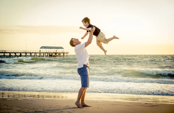 Young happy father holding up in his arms little son putting him up at the beach