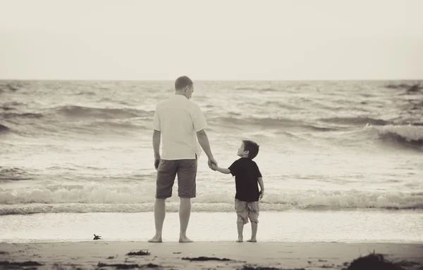 Happy father holding holding hand of little son walking together on the beach with barefoot
