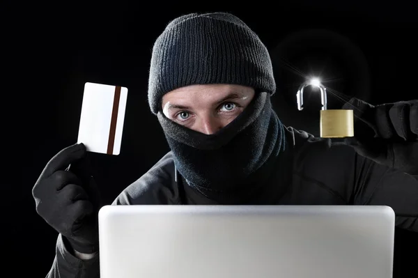 Man in black holding credit card and lock using computer laptop for criminal activity hacking bank account password