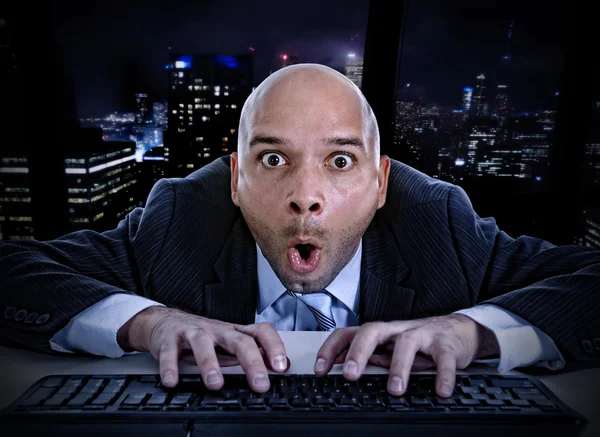 Businessman late at night in office typing on computer keyboard with funny face expression on watching porn online