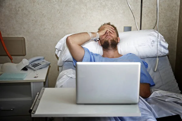 Young man in hospital room in bed using internet researching info on his own injury disease or sickness