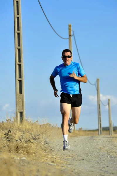 Sport man with sun glasses running on countryside track with power line poles