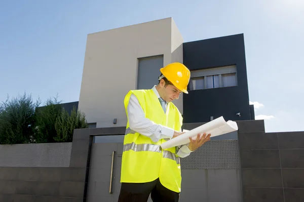 Young attractive foreman worker supervising building blueprints outdoors wearing construction helmet