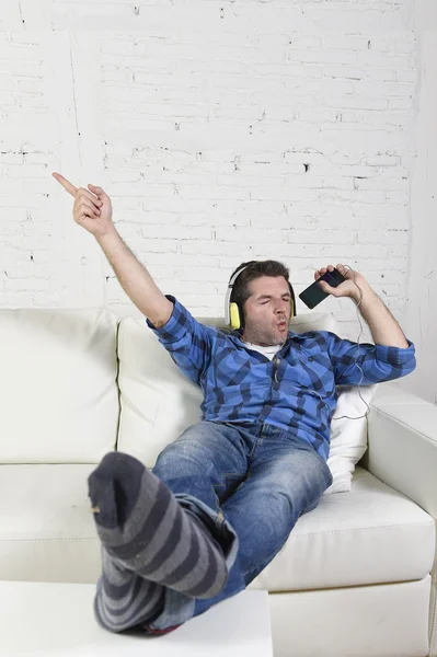 Happy crazy man on couch listening to music holding mobile phone as microphone
