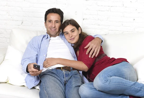 Couple in love cuddling on home couch relaxing watching movie on television with man holding remote control