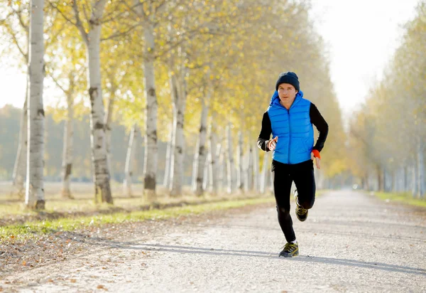 Sport man running outdoors in off road trail ground with trees under beautiful Autumn sunlight