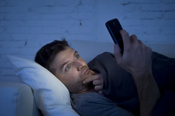 Young man in bed couch at home late at night with intense face expression using mobile phone in low light